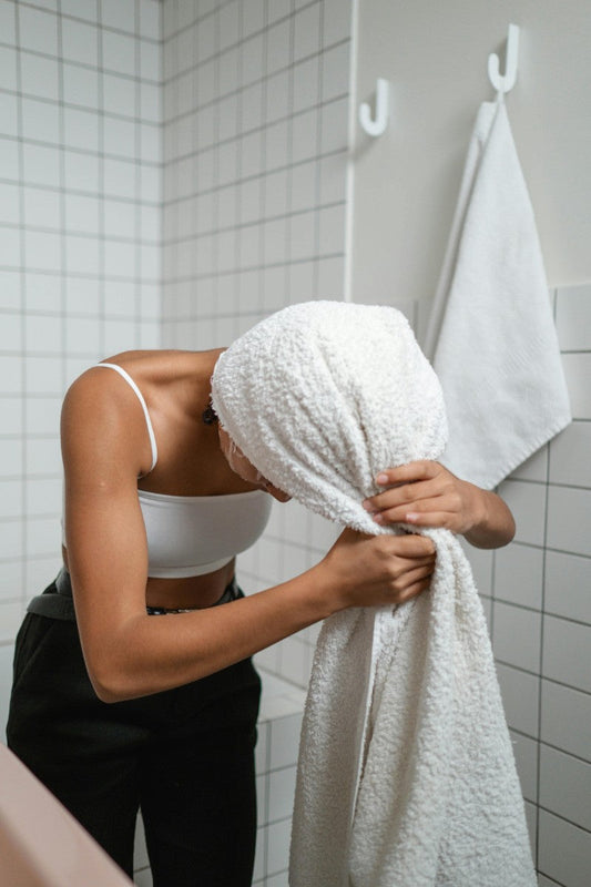 Woman drying her hair with a towel, illustrating the importance of balancing water pH to maintain moisture and prevent frizz and damage.